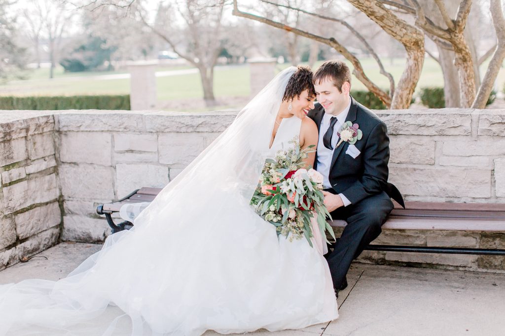 bride and groom sitting on the bench snuggling and laughing on beautiful spring day at chicago wedding venue danada house captured by bozena voytko chicago wedding photographer