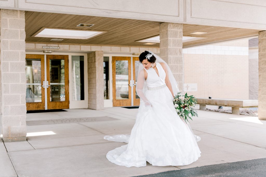 bride standing in front of the door holding wedding flowers
