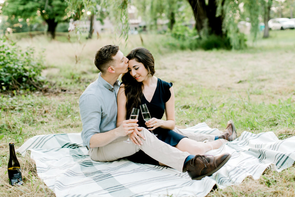 engagement session picture of girl and boy sitting on the blanket drinking champagne 