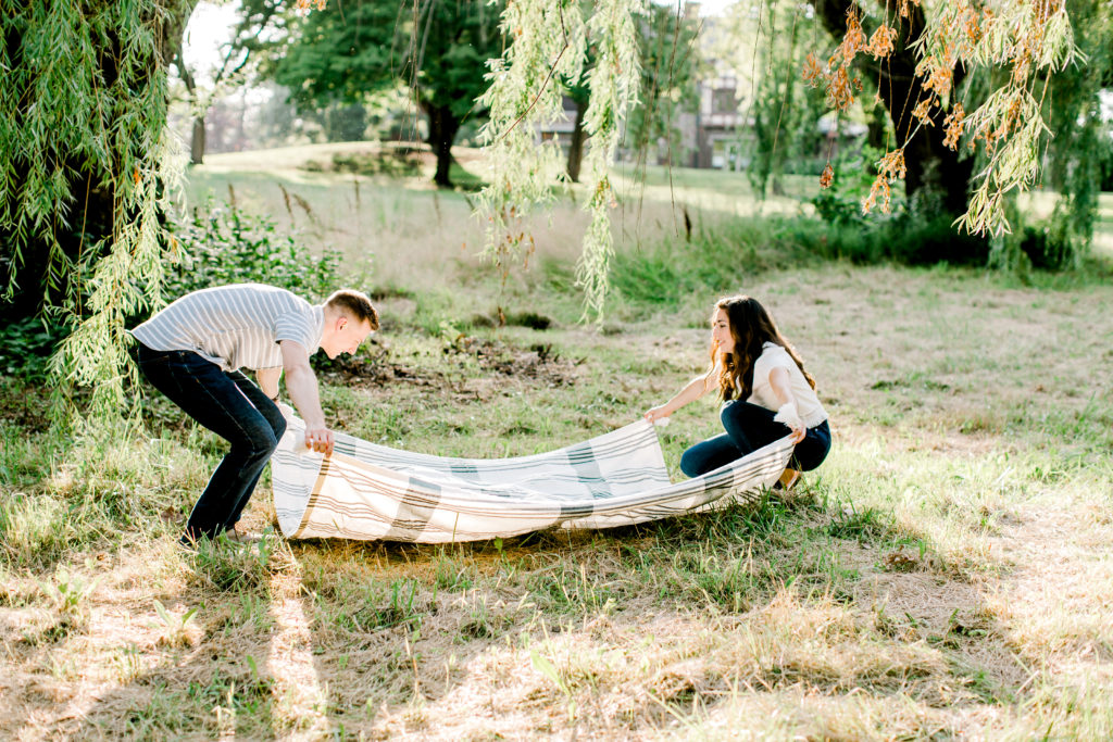 engagement session couple spreading blanket on the ground during golden hour