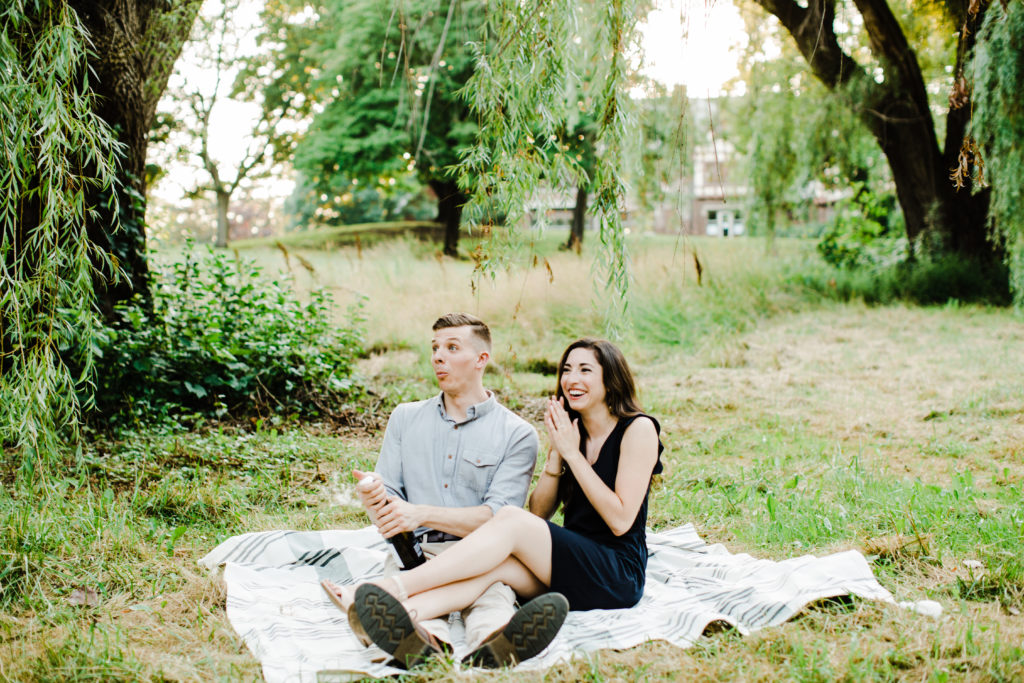 couple sitting on the grass opening bottle of champagne 