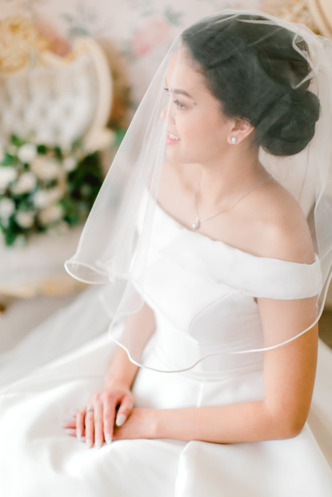 bride sitting on the chair looking away from the camera, in the background wedding bouquet on the white chair