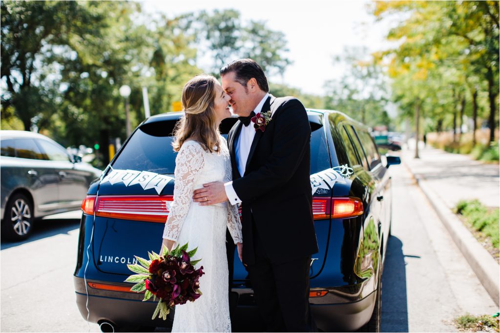bride and groom kissing in formt of the limo