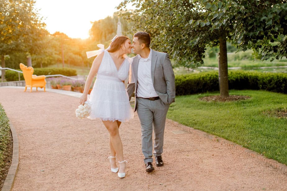 Engaged couple walking through flower-lined path at Cantigny Park, holding hands and smiling.