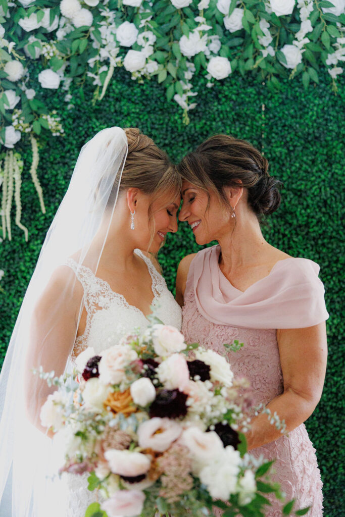 Bride and her mother standing close with foreheads touching, sharing an emotional moment.